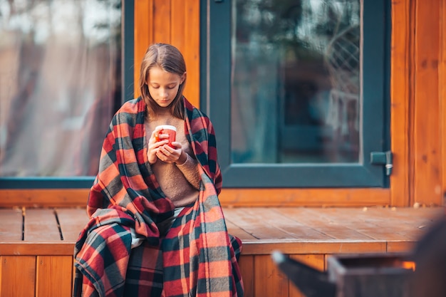 Bella ragazza con cacao caldo godendo la giornata autunnale sulla terrazza