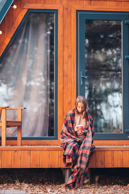 Bella ragazza con cacao caldo godendo la giornata autunnale sulla terrazza