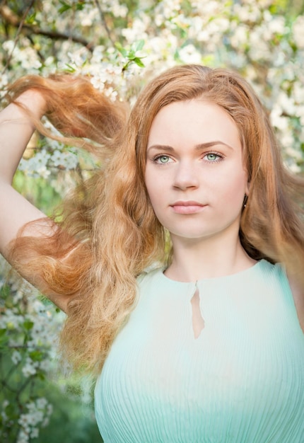 Bella ragazza con capelli biondi nel giardino fiorito di primavera