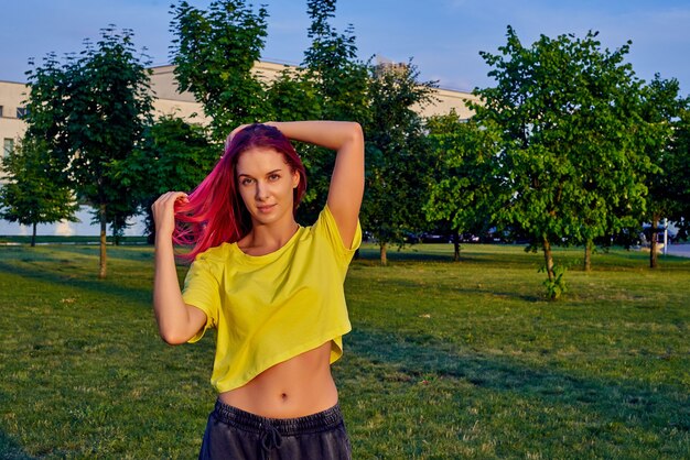 Bella ragazza con capelli rosa tinti, top corto giallo nel parco cittadino