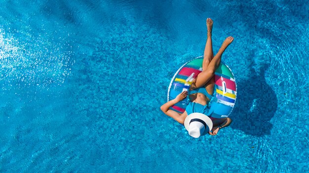 Bella ragazza con cappello in piscina vista aerea drone dall'alto, la donna si rilassa e nuota sulla ciambella ad anello gonfiabile e si diverte in acqua in vacanza con la famiglia, località di villeggiatura tropicale