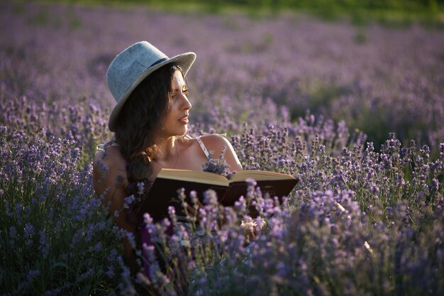 Bella ragazza con cappello seduto nel campo di lavanda viola e leggere il libro