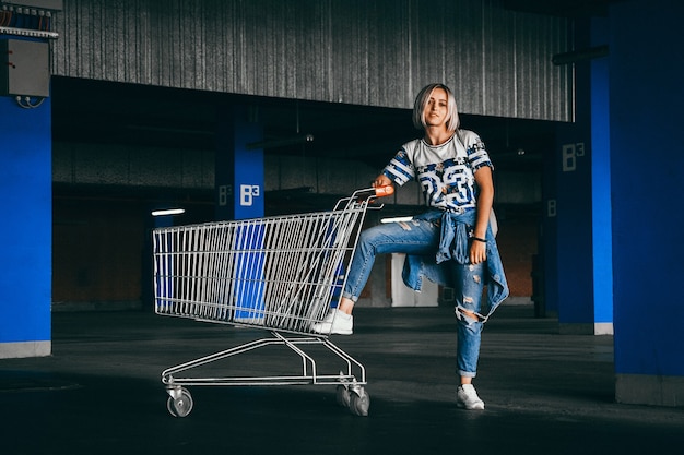 Bella ragazza con corti capelli bianchi vestita di jeans con carrelli della spesa nel parcheggio