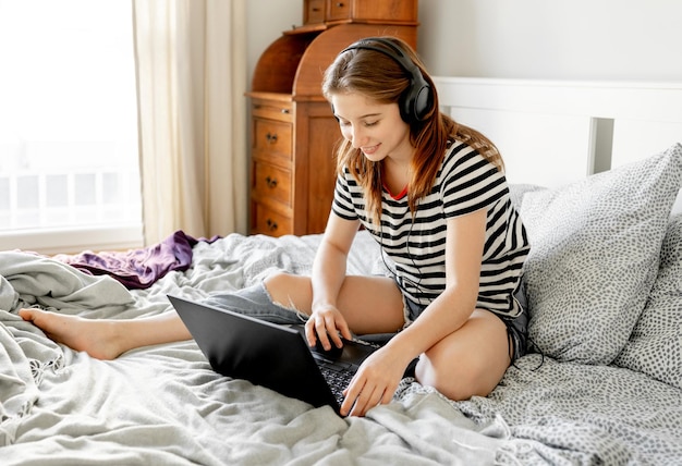 Bella ragazza con cuffie e laptop a letto