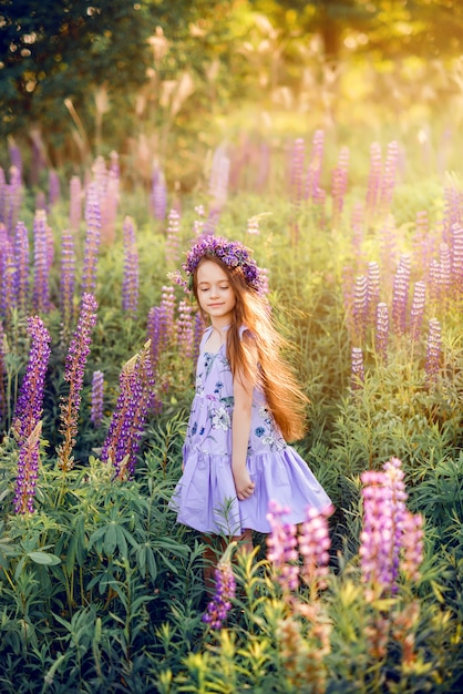 Bella ragazza con fiori tra i capelli tra i fiori. Foto di sole estivo con un bambino in fiori viola