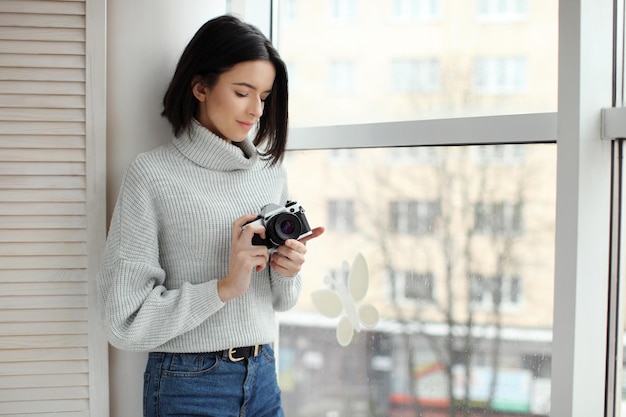 Bella ragazza con fotocamera vintage alla finestra