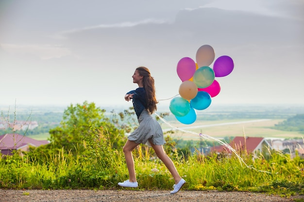 Bella ragazza con grandi palloncini colorati che cammina sulle colline vicino alla città