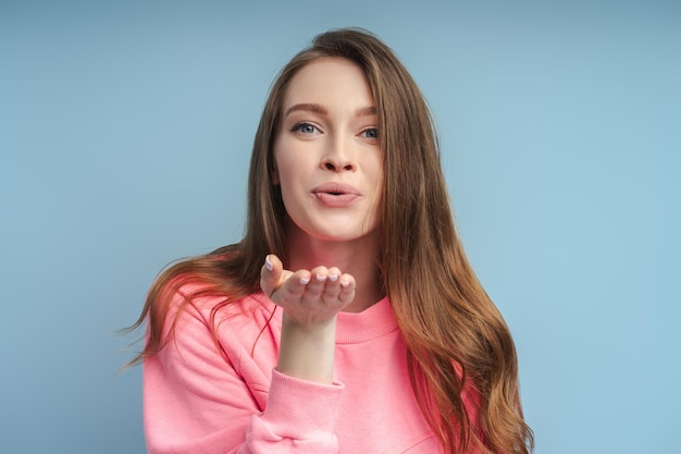 bella ragazza con i capelli lunghi che mostra l'aria bacio gesticolando isolato sullo sfondo blu