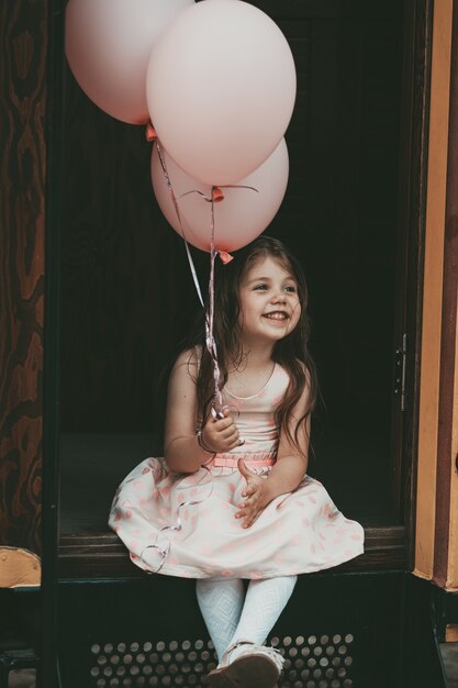 Bella ragazza con i capelli lunghi in un vestito rosa esce dal tram con palloncini in mano. Foto di alta qualità