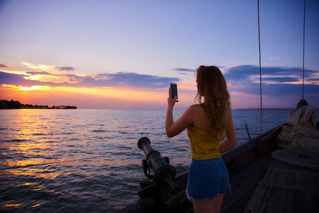 Bella ragazza con i capelli lunghi incontra l'alba. Barca a vela nel mare al tramonto