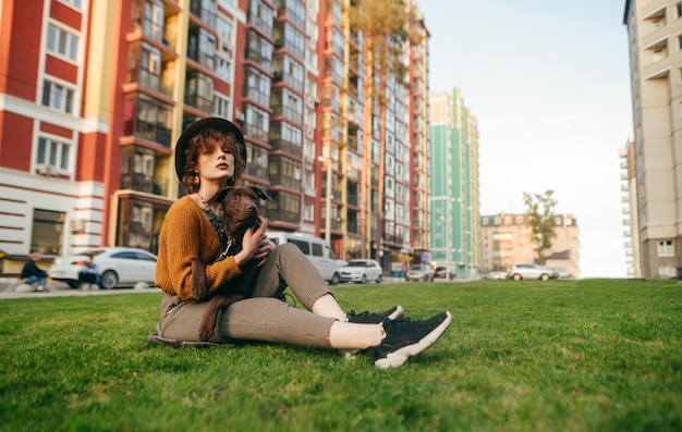 Bella ragazza con i capelli ricci e un cane in mano si siede in cortile