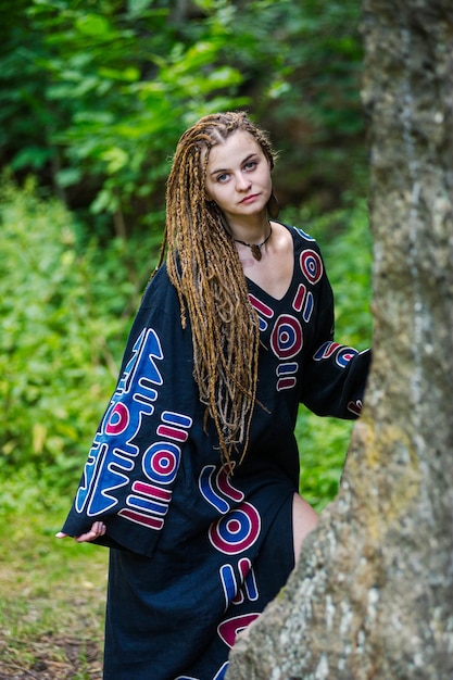 Bella ragazza con i dreadlocks vestita in stile hippie posa all'aperto