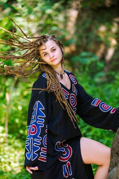 Bella ragazza con i dreadlocks vestita in stile hippie posa all'aperto