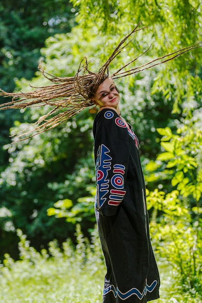 Bella ragazza con i dreadlocks vestita in stile hippie posa all'aperto