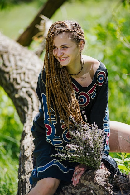 Bella ragazza con i dreadlocks vestita in stile hippie posa all'aperto