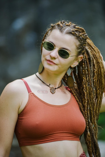 Bella ragazza con i dreadlocks vestita in stile hippie posa all'aperto