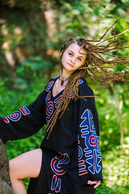 Bella ragazza con i dreadlocks vestita in stile hippie posa all'aperto