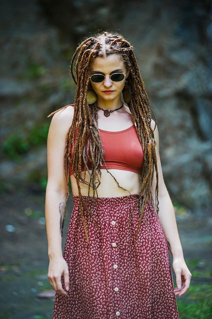 Bella ragazza con i dreadlocks vestita in stile hippie posa all'aperto