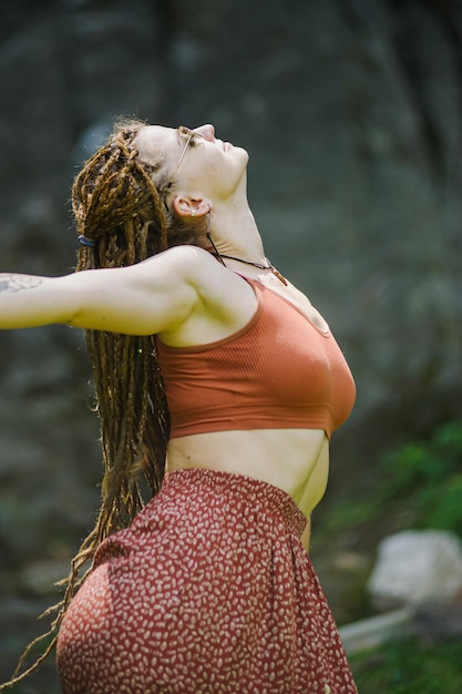 Bella ragazza con i dreadlocks vestita in stile hippie posa all'aperto