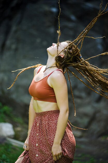 Bella ragazza con i dreadlocks vestita in stile hippie posa all'aperto