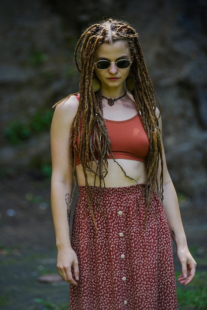 Bella ragazza con i dreadlocks vestita in stile hippie posa all'aperto