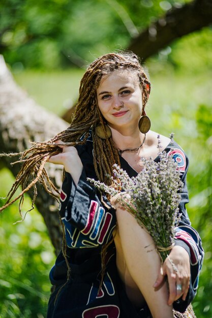 Bella ragazza con i dreadlocks vestita in stile hippie posa all'aperto