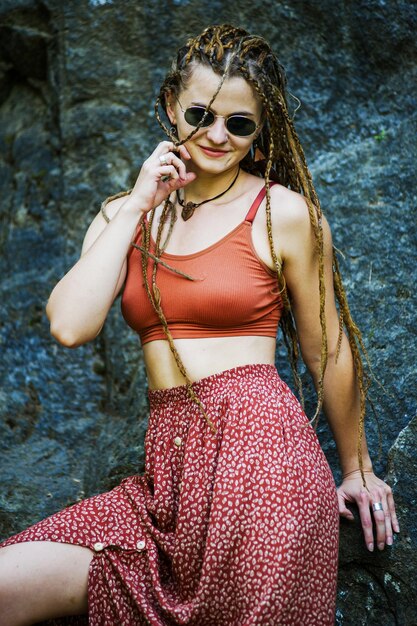 Bella ragazza con i dreadlocks vestita in stile hippie posa all'aperto