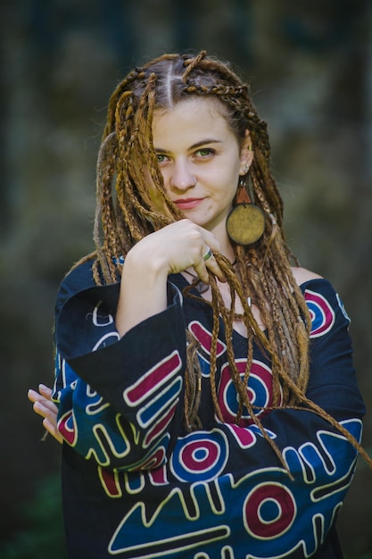 Bella ragazza con i dreadlocks vestita in stile hippie posa all'aperto