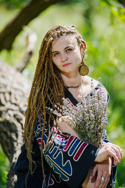 Bella ragazza con i dreadlocks vestita in stile hippie posa all'aperto