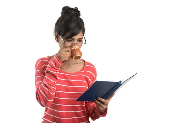 Bella ragazza con il libro e la tazza di caffè in posa su un muro bianco.