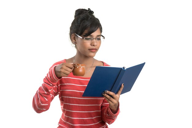 Bella ragazza con il libro e la tazza di caffè in posa su un muro bianco.