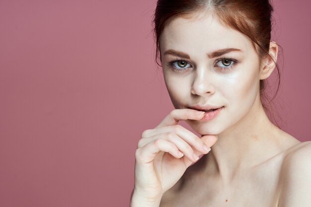 Bella ragazza con il modello del viso della pelle pulita in posa sorridente su sfondo rosa isolato