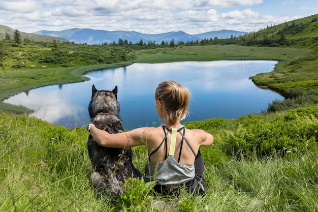 Bella ragazza con il suo adorabile cane husky siberiano che fa un'escursione nel lago di montagna blu in montagna