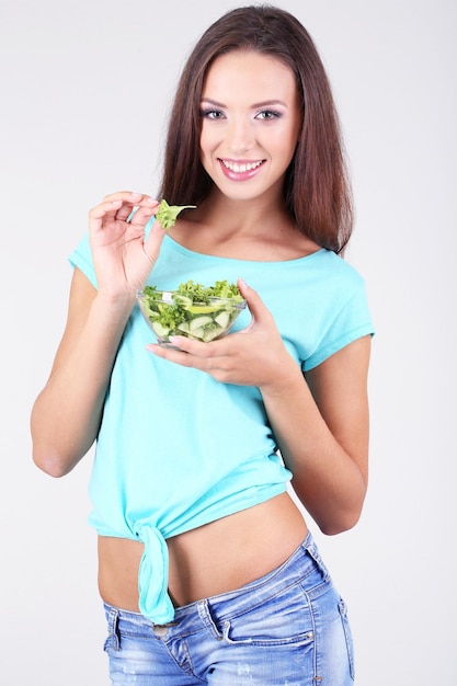 Bella ragazza con insalata fresca su sfondo grigio