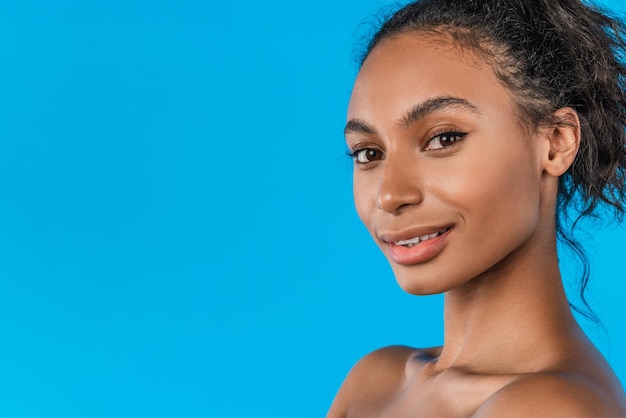 Bella ragazza con l'acconciatura afro sorridente alla telecamera su sfondo blu