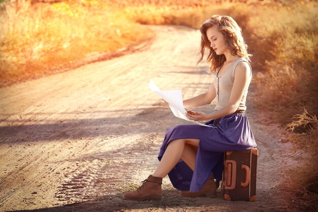 Bella ragazza con la mappa che si siede sulla valigia