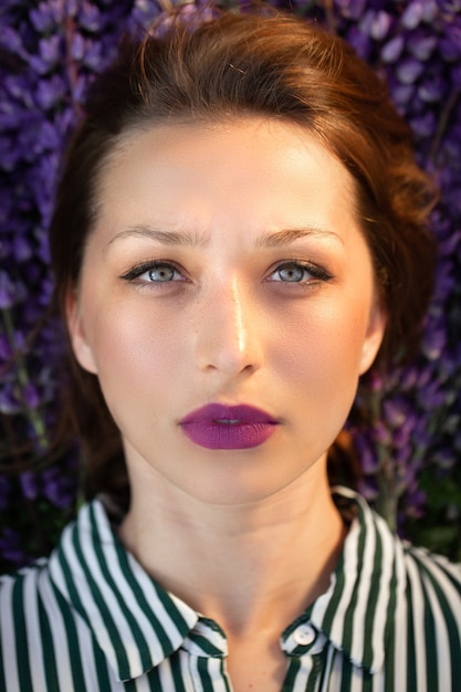 Bella ragazza con le labbra lilla che si trovano sullo sfondo di fiori viola nei raggi del tramonto