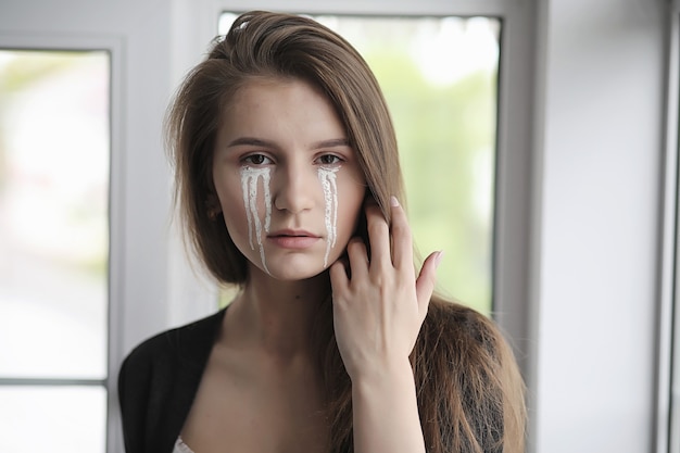 Bella ragazza con le lacrime agli occhi. Ragazza giovane con lacrime dipinte in posa sulla macchina fotografica. Ragazza per carnevale con maschera e trucco.