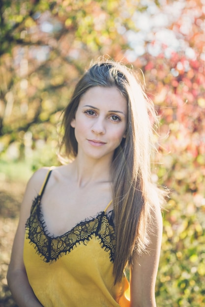 Bella ragazza con lunghi sani capelli biondo scuro in un top di seta gialla in un parco in autunno, sorridendo alla telecamera