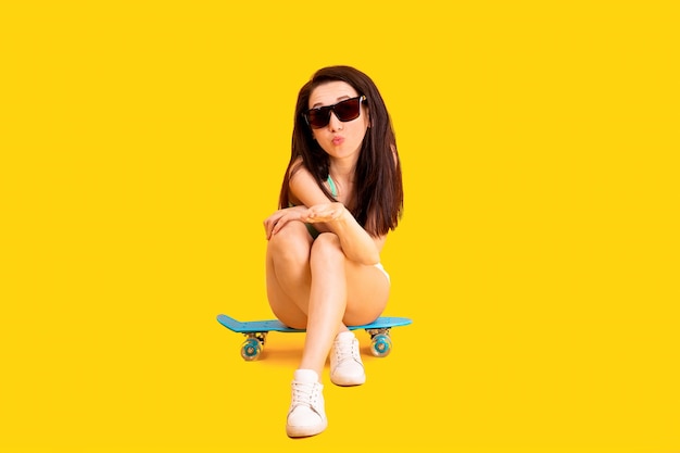 Bella ragazza con occhiali da sole seduto su uno skateboard