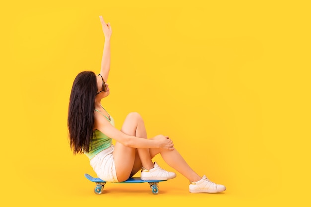 Bella ragazza con occhiali da sole seduto su uno skateboard