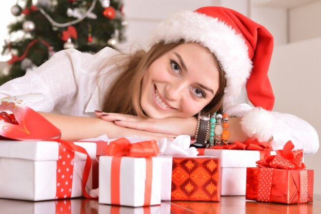 Bella ragazza con regali vicino all'albero di Natale in santa hat