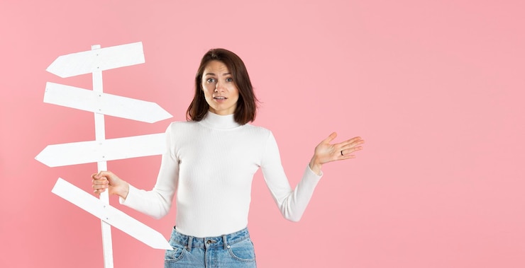 Foto bella ragazza con segnali stradali bianchi in mano isolati su sfondo rosa