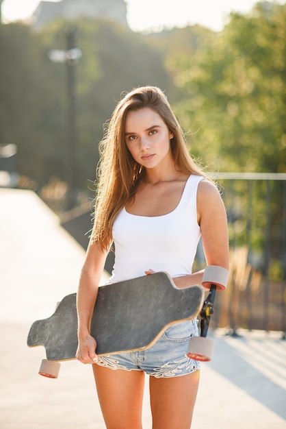 Bella ragazza con skateboard nelle mani contro il muro