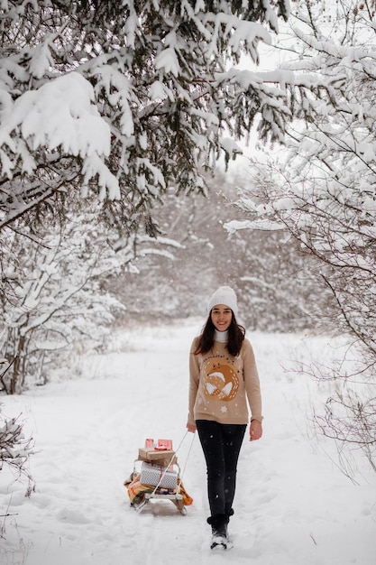 Bella ragazza con slitte albero di Natale e regali in inverno in un bosco innevato