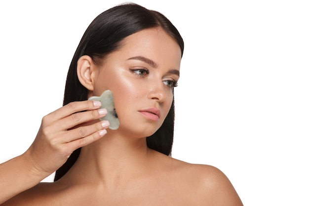 Bella ragazza con trucco naturale e pelle pulita Tiene in mano uno scrubber viso giada