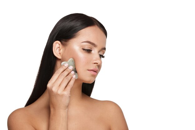 Bella ragazza con trucco naturale e pelle pulita Tiene in mano uno scrubber viso giada