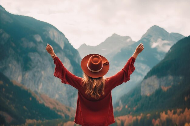 bella ragazza con un cappello alza le mani in aria contro lo sfondo delle montagne vista posteriore