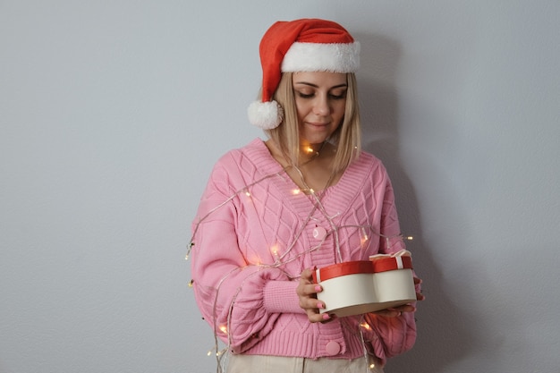 Bella ragazza con un cappello di Babbo Natale, decorata con lanterne di Capodanno con un regalo in mano, primo piano. Il concetto di Natale e Capodanno.