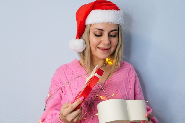 Bella ragazza con un cappello di Babbo Natale, decorata con lanterne di Capodanno con un regalo in mano, primo piano. Il concetto di Natale e Capodanno.